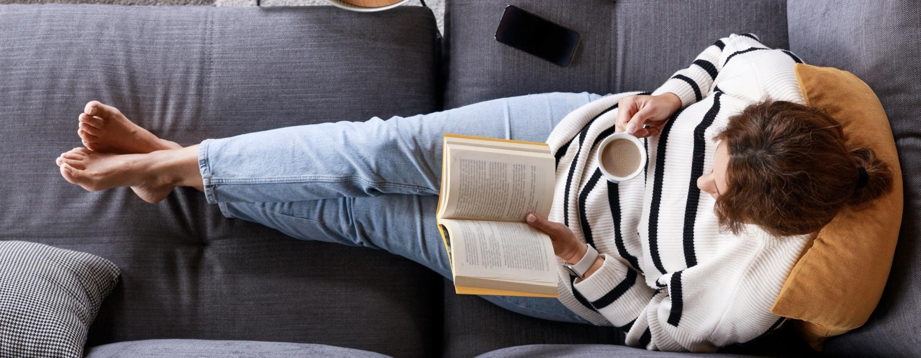 a person lying on a couch reading a book